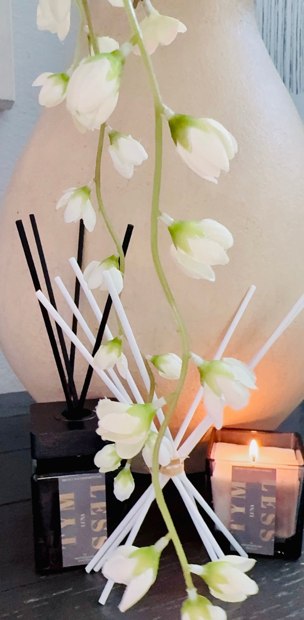 Reed diffuser with black and white sticks, candle, and white flower decoration