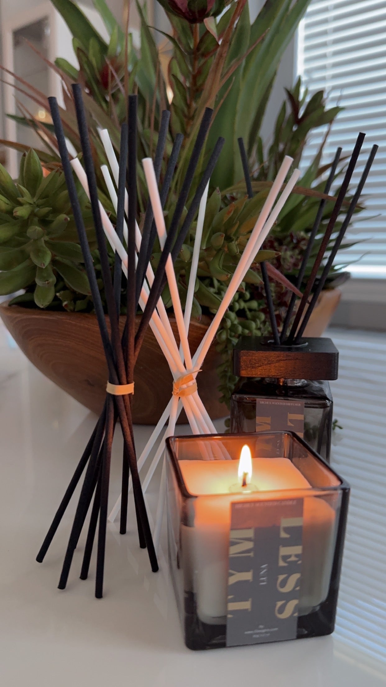Reed diffuser with black and white sticks next to a lit candle.